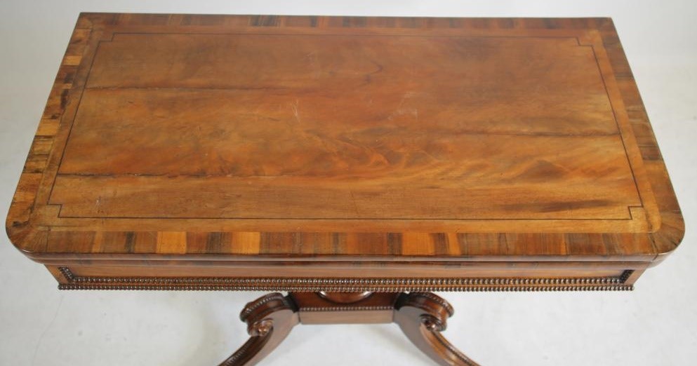 A REGENCY MAHOGANY FOLDING CARD TABLE of rounded oblong form with stringing and beaded edging Image