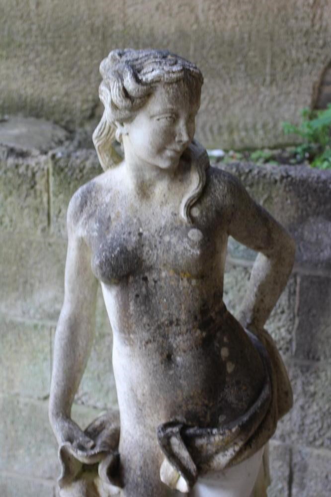 A CAST STONE FIGURE OF A WATER NYMPH, the nude figure standing and holding a shell, another shell at Image