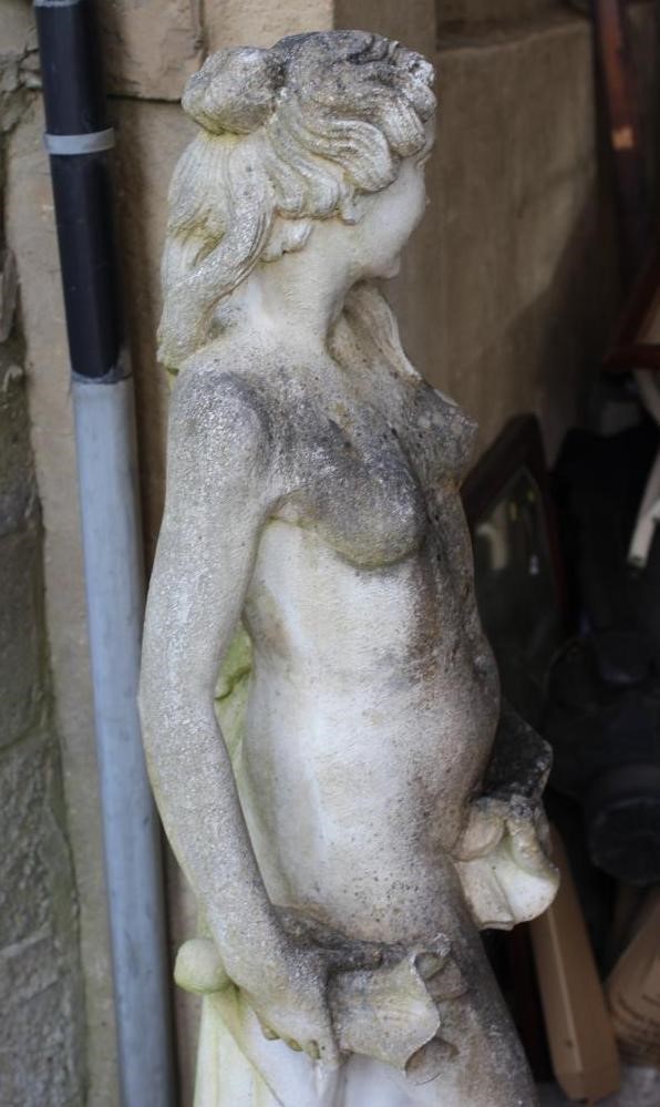 A CAST STONE FIGURE OF A WATER NYMPH, the nude figure standing and holding a shell, another shell at Image