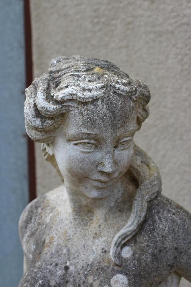 A CAST STONE FIGURE OF A WATER NYMPH, the nude figure standing and holding a shell, another shell at Image