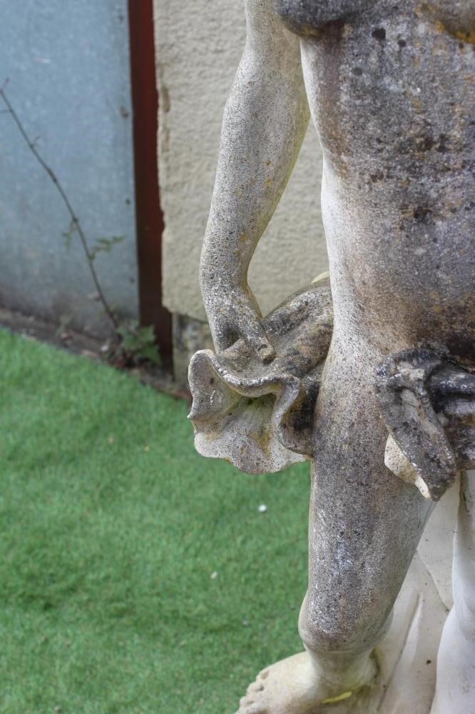 A CAST STONE FIGURE OF A WATER NYMPH, the nude figure standing and holding a shell, another shell at Image